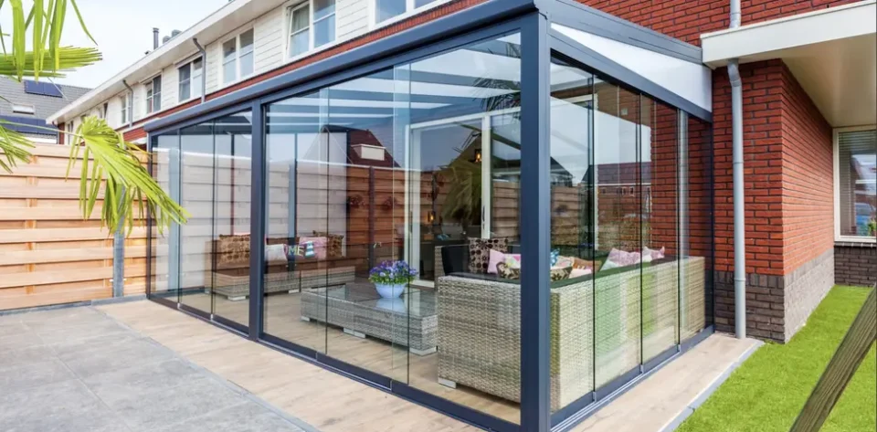 Anthracite Grey frame glass room veranda with glass sliding doors, furnished with light brown garden rattan sofas and coffee table.