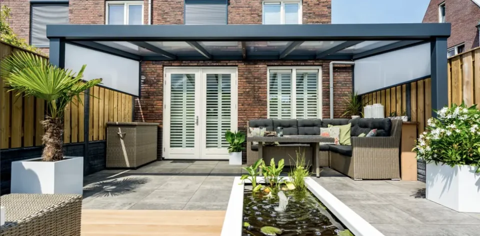 Anthracite Grey frame veranda with a glass roof, LED spot lights and 2 ash grey side awnings, furnished with light brown rattan garden sofas, coffee table and storage.