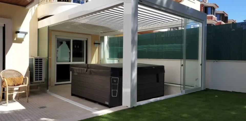 White frame bioclimatic pergola with glass sliding doors and a brown covered jacuzzi
